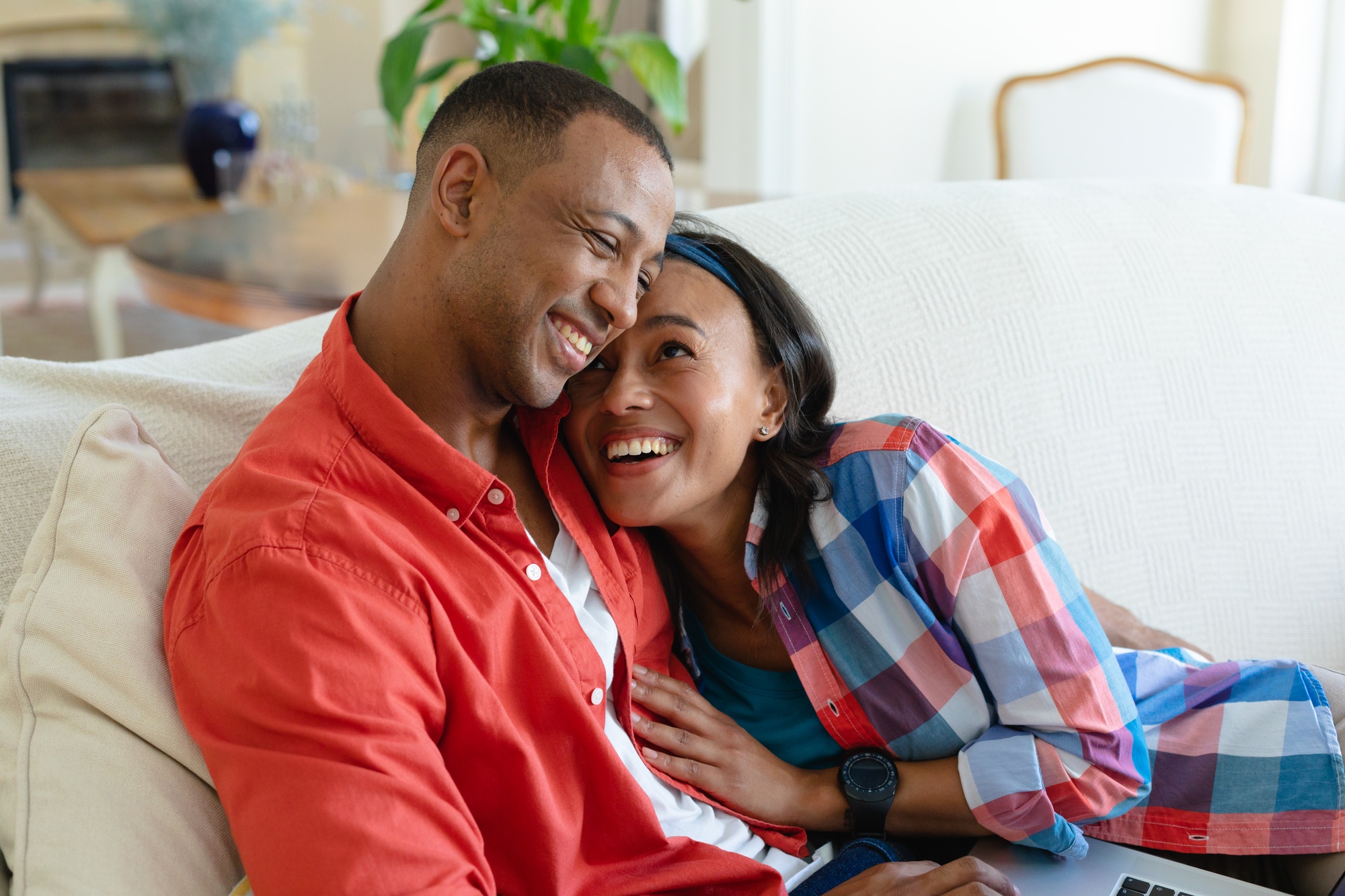 Happy african american young couple lying with laptop on sofa at home